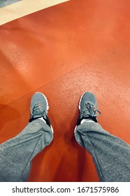 Male Feet In Sports Shoes Are Over Red Gym Floor, First Person View