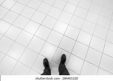 Male Feet Stand On Office Floor With White Shining Square Tiling