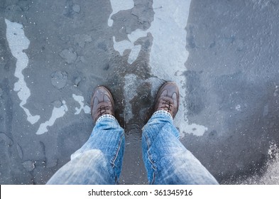 Male Feet Standing On Frozen Puddle With Thin Ice And Falling Leaves