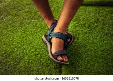 Male feet wearing sport sandals on the artificial grass carpet. Sandal on feet selective focus