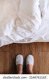 Male Feet In White Hotel Slippers Standing In Front Of The Bed, Top View