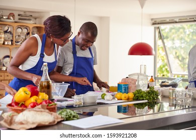 Male And Female Adult Students Looking At Recipe In Cookery Class In Kitchen