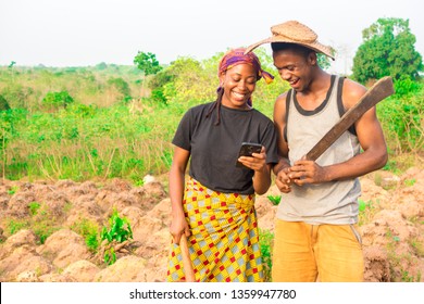 Male And Female African Farmers On A Farm Smiling While Viewing Something On A Phone Together