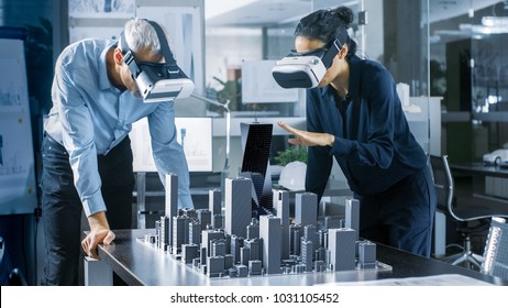 Male And Female Architects Wearing  Augmented Reality Headsets Work With 3D City Model. High Tech Office Professional People Use Virtual Reality Modeling Software Application.