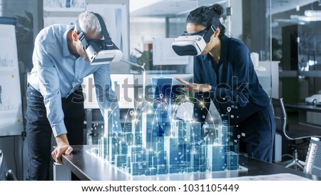 Male and Female Architects Wearing  Augmented Reality Headsets Work with 3D City Model. High Tech Office Professional People Use Virtual Reality Modeling Software Application.