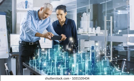 Male And Female Architects Work With Holographic Augmented Reality 3D City Model. Technologically Advanced Office Professional People Use Virtual Reality Modeling Software Application.