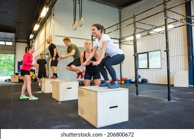 Male and female athletes doing box jumps at gym