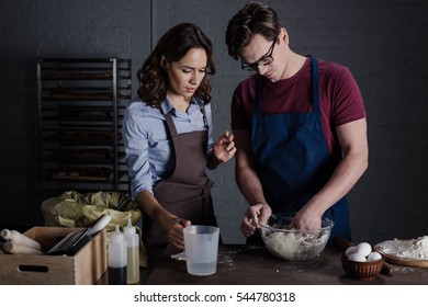 Male and female bakers discussing ingredients and kneading dough in bakehouse  - Powered by Shutterstock