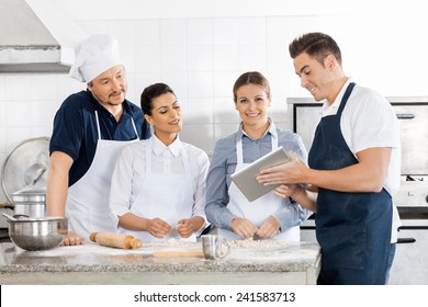 Male and female chefs checking recipe on tablet computer while preparing pasta in commercial kitchen - Powered by Shutterstock