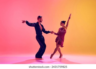 Male and female dancers performing a Latin dance in stylish clothes against gradient pink yellow background in neon light. Concept of dance class, hobby, art, dance school, talent - Powered by Shutterstock