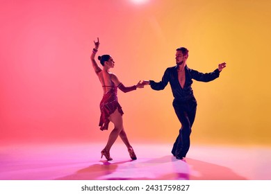 Male and female dancers performing a Latin dance in stylish clothes against gradient pink yellow background in neon light. Concept of dance class, hobby, art, dance school, talent - Powered by Shutterstock