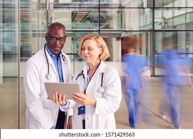 Male And Female Doctors Having Informal Meeting In Modern Hospital Looking At Digital Tablet