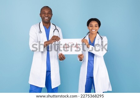 Male and female doctors in white medical gown suits holding paper with drawn heart rate electrocardiogram record cardiogram chart, standing on blue background. Healthcare medicine concept