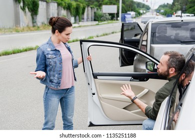 male and female drivers quarreling and gesturing on road after car accident