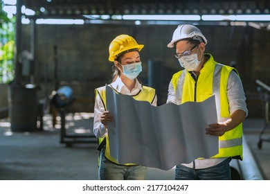 Male And Female Engineers Spreading The Floor Plan Inside The Factory And Discussing To Plan The Installation Of New Types Of Machines