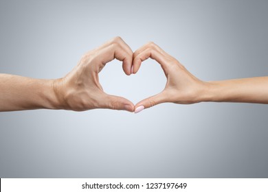 Male and female hands forming a heart shape on grey background