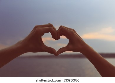 Male and female hands forming heart on blue sky background, close up view