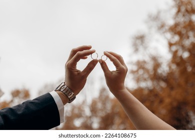 Male and female hands as silhouettes hold wedding rings facing each other. The bride and groom put their wedding rings against the sky. Weddings and gold wedding rings.