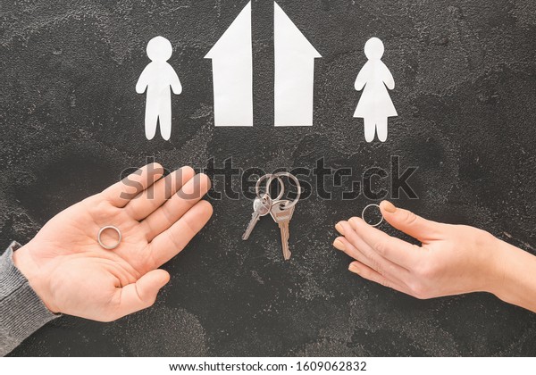 Male and\
female hands with wedding rings, keys, cut figures of house and\
couple on dark background. Concept of\
divorce