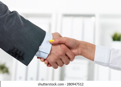 Male And Female Handshake In Office. Businessman In Suit Shaking Woman's Hand. Serious Business And Partnership Concept. Partners Made Deal And Sealed It With Handclasp. Formal Greeting Gesture