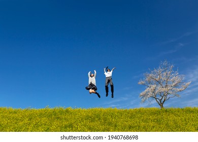 Male And Female High School Students Jumping On Bank Of Rape Blossoms And Cherry Blossoms. Spring, Admission, Celebration, Graduation, Passing Exam, Image 