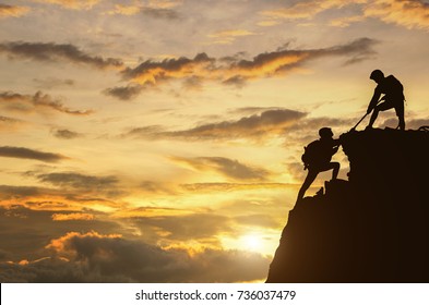 Male And Female Hikers Climbing Up Mountain Cliff And One Of Them Giving Helping Hand. People Helping And, Team Work Concept. 