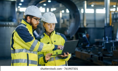 Male   Female Industrial Engineers in Hard Hats Discuss New Project while Using Laptop  They Make Showing Gestures They Work in Heavy Industry Manufacturing Factory 