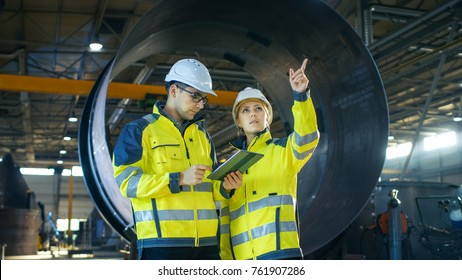 Male and Female Industrial Engineers Have Discussion while Using Tablet Computer. They Work in a Heavy Industry Manufacturing Factory. - Powered by Shutterstock