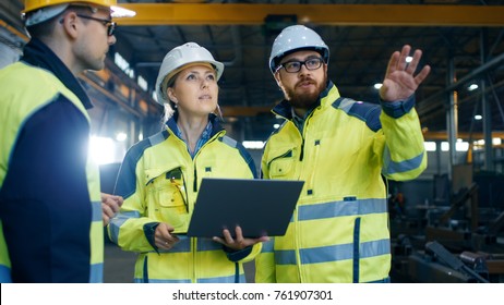 Male and Female Industrial Engineers Talk with Factory Worker while Using Laptop. They Work at the Heavy Industry Manufacturing Facility.