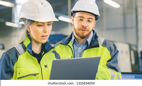 Male And Female Industrial Engineers Work On A Manufacturing Plant, They Discuss Project, Point In The Direction Of The Machinery While Using Laptop.