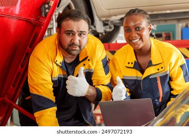 Male and female mechanics smiling and giving thumbs up while working on a red car engine in a garage. Wearing yellow and blue uniforms. Emphasizes satisfaction, teamwork, and successful repair outcome - Powered by Shutterstock