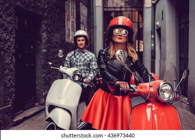 Male and female on motor scooters in a town.