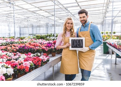 Male and female owners of glasshouse holding Open board by flowers - Powered by Shutterstock