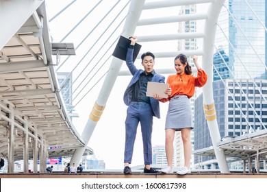 The Male And Female Partner Workers Are Very Happy. They Lifted Their Fists And Had A Bright Face. With The Backdrop Of A Tall Building In The Morning The Concept Of Success Is Being Raised In Stock