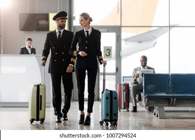 male and female pilots walking by airport lobby with suitcases