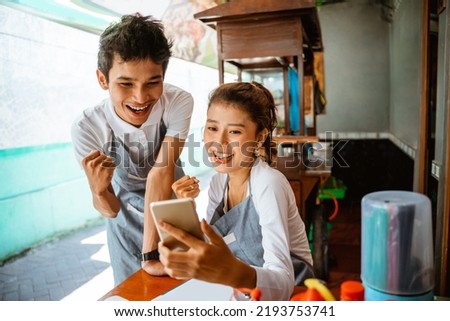 male and female sellers are excited to use mobile phones together at a chicken noodle shop