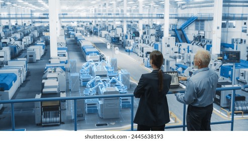 Male and Female Standing at Electronics Factory, Using Computer and Having a Conversation. Augmented Reality Visualization of a Conveyor Belt Production Line with Robot Arms Appears In Front of Them - Powered by Shutterstock