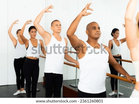 Male and female students at performing arts school rehearsing ballet in dance studio using barre
