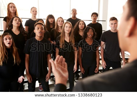 Male And Female Students Singing In Choir With Teacher At Performing Arts School