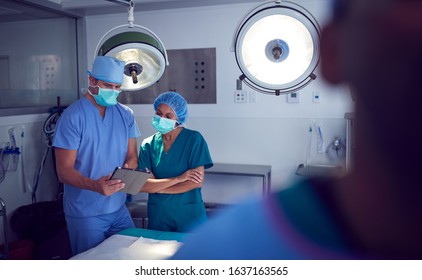 Male And Female Surgeons Wearing Scrubs Looking At Digital Tablet In Hospital Operating Theater - Powered by Shutterstock