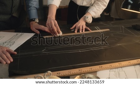 Male and female tailors transfer the sketch of future clothes to the fabric. They use ruler, soap and buttons. Luxury designer atelier or tailoring dim studio. Fashion, hand craft and handmade concept