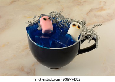 Male And Female Or White And Pink Marshmallows With Toy Doll Eyes And Gray Crinkled Shredded Paper Hair In A Sea Of Blue Blueberry Gelatin In Coffee Cup