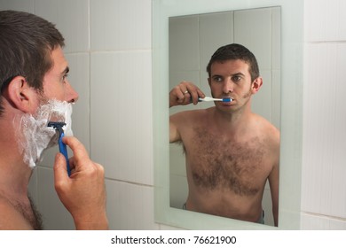 A Male Figure Multi Tasking, Shaving And Brushing Teeth Reflected In A Bathroom Mirror