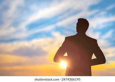 male figure silhouette businessman by setting sun, backdrop of blue and orange sky with soft clouds marking end of day - Powered by Shutterstock