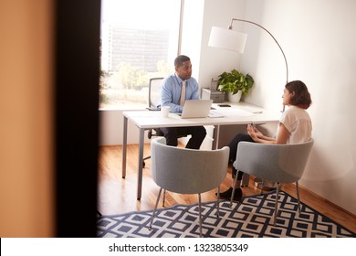 Male Financial Advisor In Modern Office Sitting At Desk Meeting Female Client