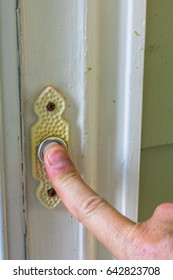 Male Finger Ringing A Doorbell To A Front Door With A White Frame On A Green House