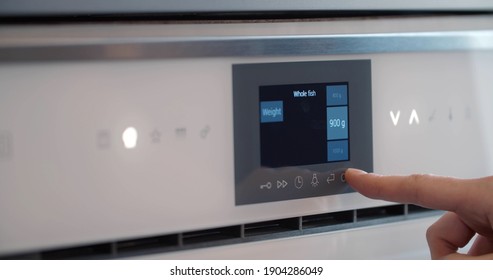 Male Finger Touching Button Of Modern Panel Of Electric Oven. Close Up Of Person Selecting Cooking Regime On Screen Of Modern Microwave Cooking Dinner In Kitchen