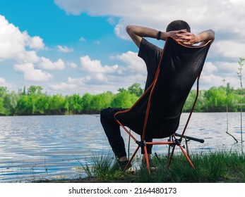 A Male Fisherman Is Fishing With A Float Rod, Sitting In A Folding Chair. Outdoor Recreation And Hobbies