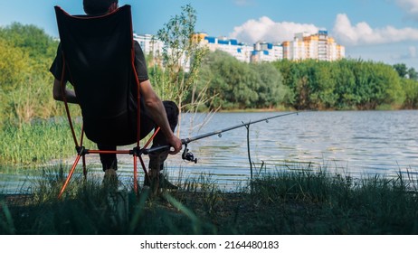 A Male Fisherman Is Fishing With A Float Rod, Sitting In A Folding Chair. Outdoor Recreation And Hobbies