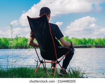 A Male Fisherman Is Fishing With A Float Rod, Sitting In A Folding Chair. Outdoor Recreation And Hobbies